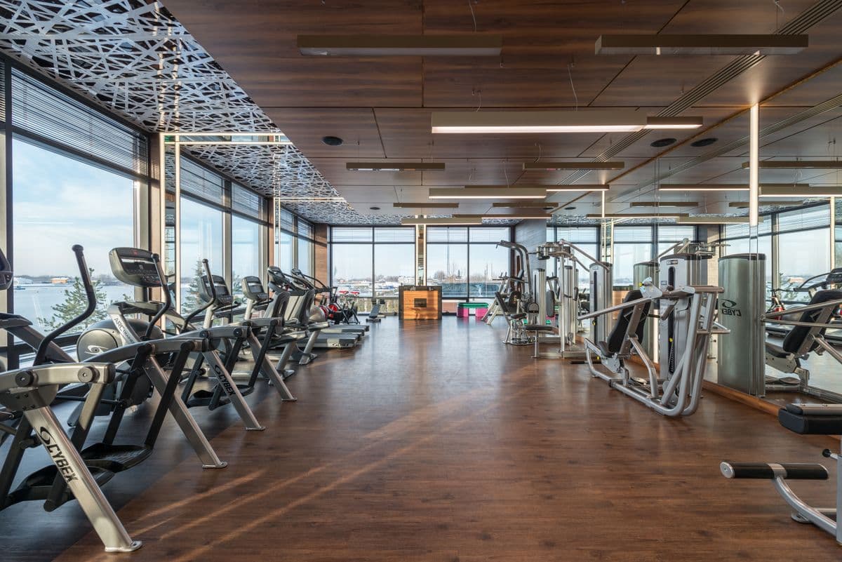 Gym floor with a row of treadmills and cross-trainers facing resistance machines