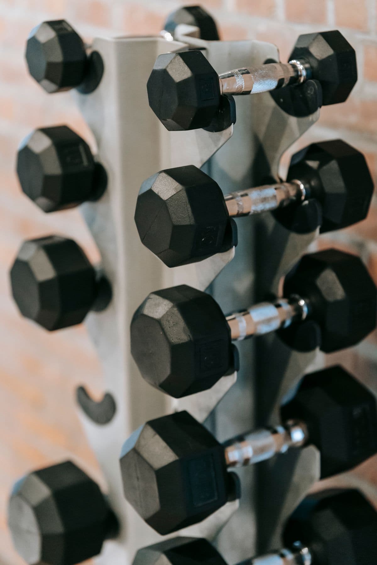 Hex dumbbells racked in pairs against an exposed brick wall