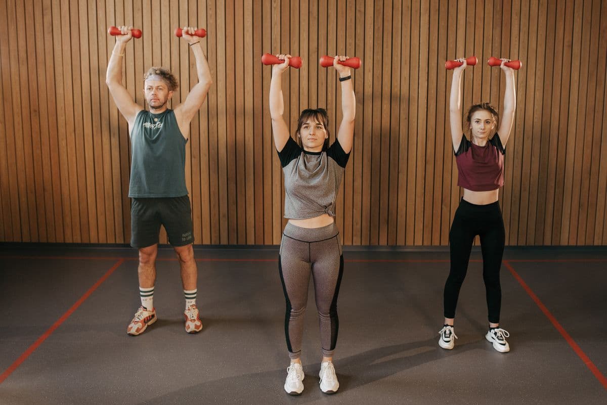 Three members pressing dumbbells overhead together during a group class
