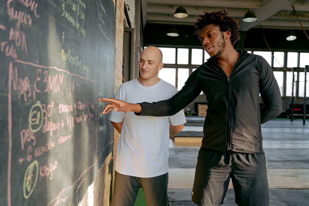 Coach talking a member through a training programme written out on a gym chalkboard